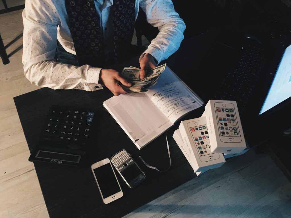 Businessman organizing finances with tech devices and cash on desk.